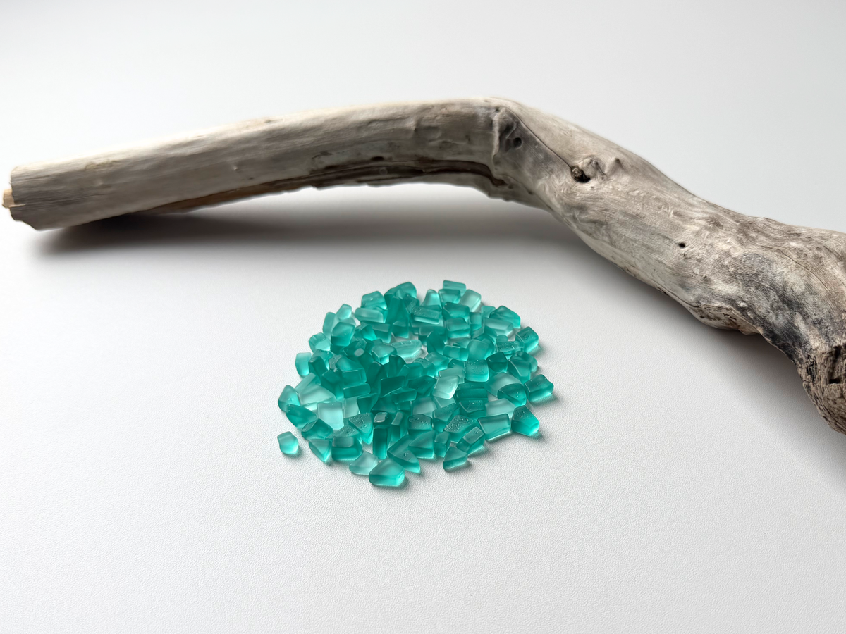 Small pile of aqua micro sea glass pieces on a driftwood branch background.