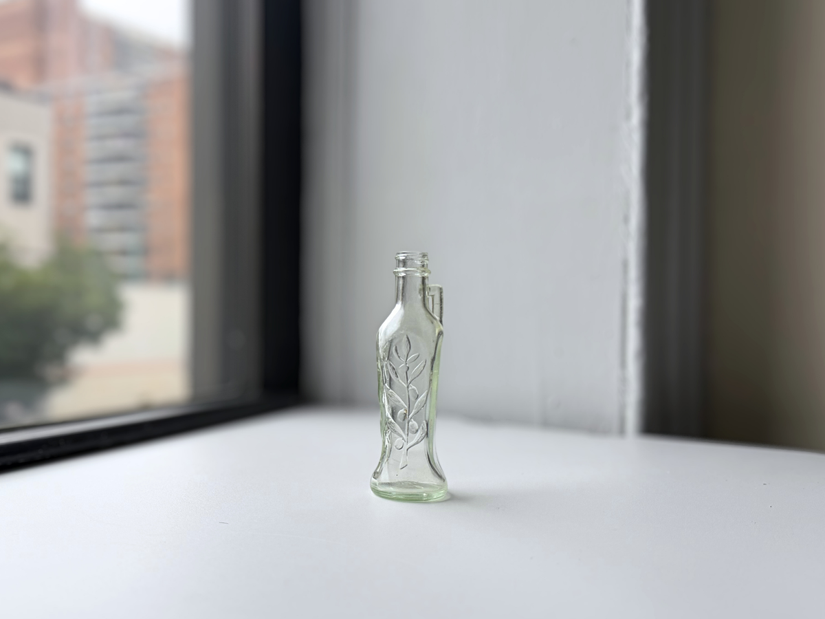 Clear glass Bon Oil bottle with integrated neck handle displayed on a windowsill, 1940s.