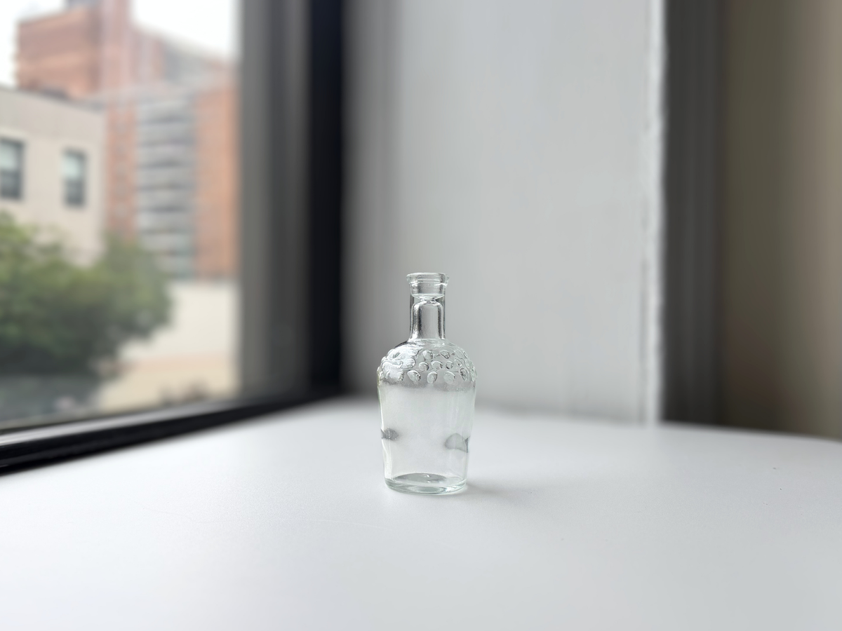 Clear glass hobnail bud vase with stopper displayed on a windowsill.