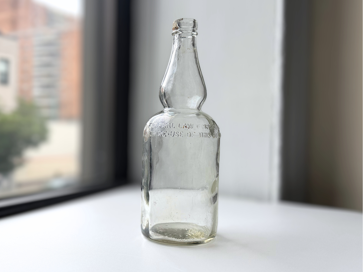Clear glass James Martin & Co. whiskey bottle with a tapered bulbous neck, displayed on a sunlit windowsill.