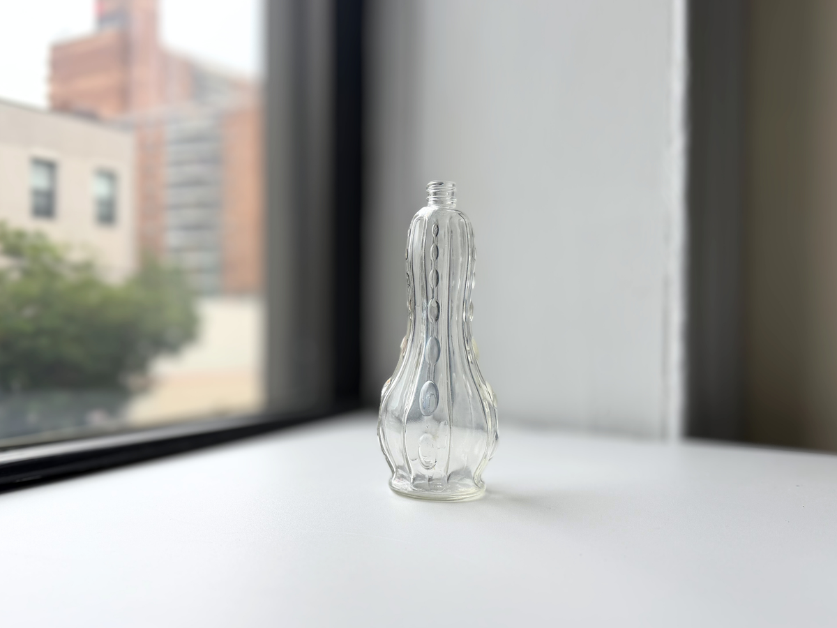 Clear glass teardrop-shaped bottle with raised bump texture displayed on a windowsill.