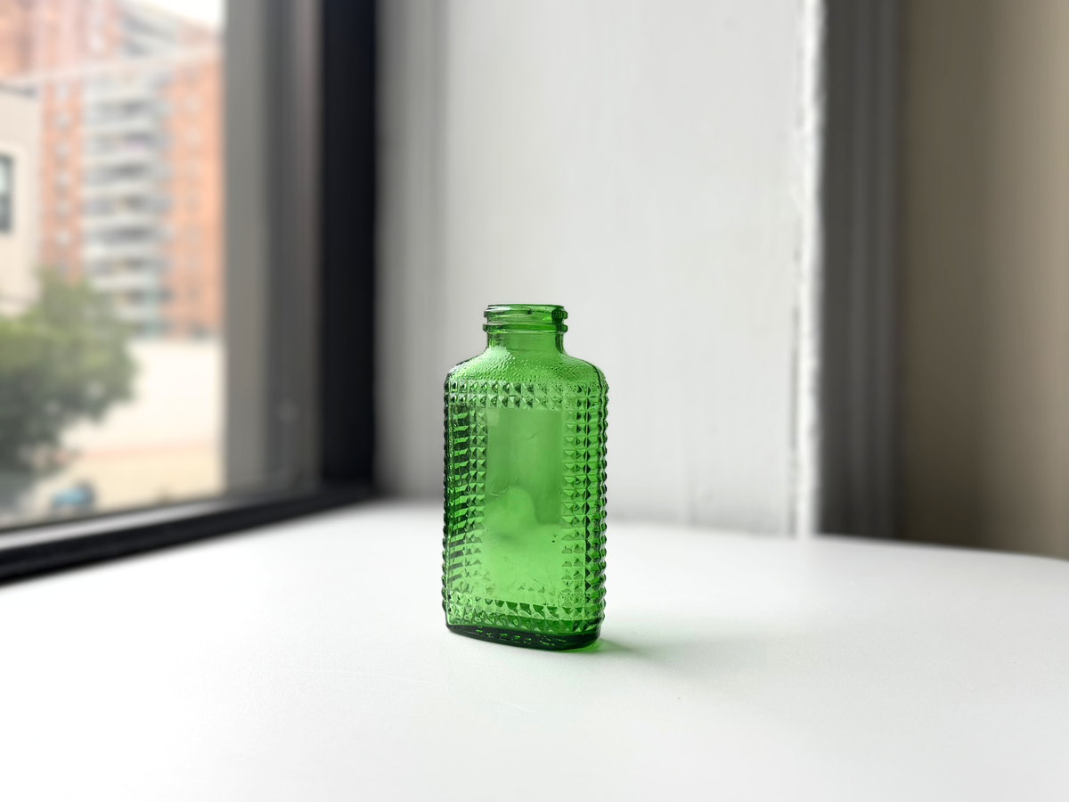 Vintage kelly green Airwick hobnail glass bottle sitting on a windowsill, front view