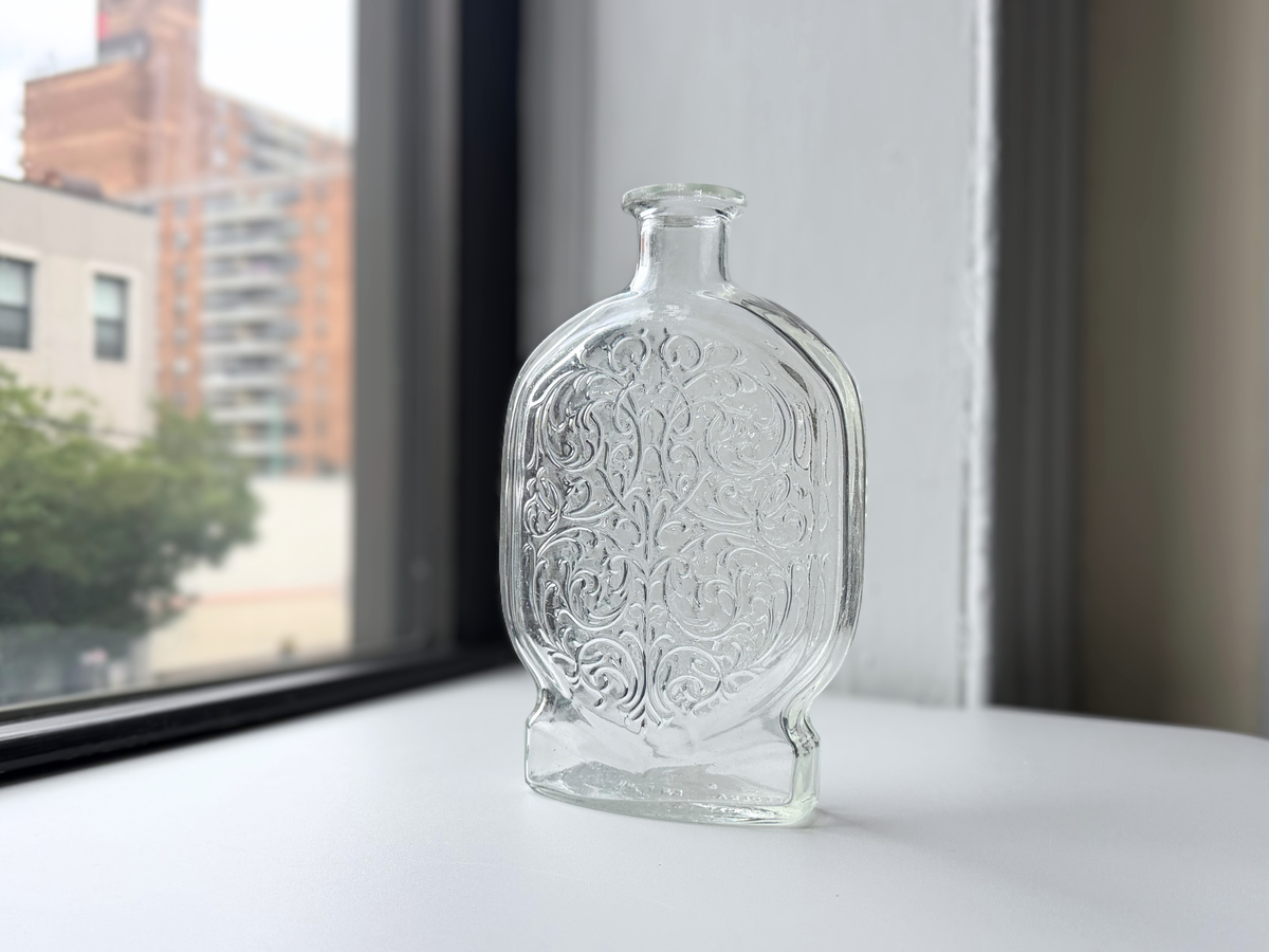 Schenley clear glass decanter with Art Nouveau scrollwork displayed on a windowsill, 1950s.