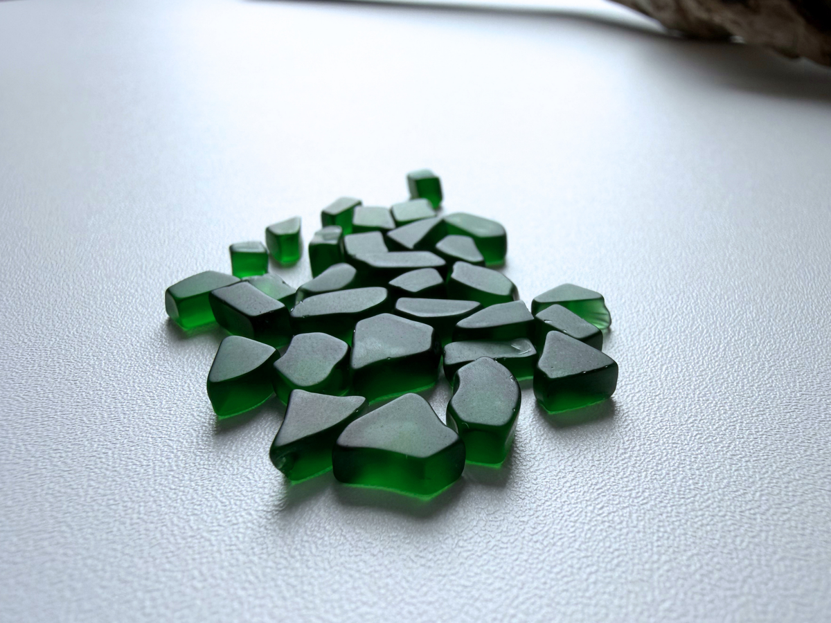Abundant pile of dark green micro sea glass filler pieces spread across a white background, showing the deep forest green color and small tumbled shapes.