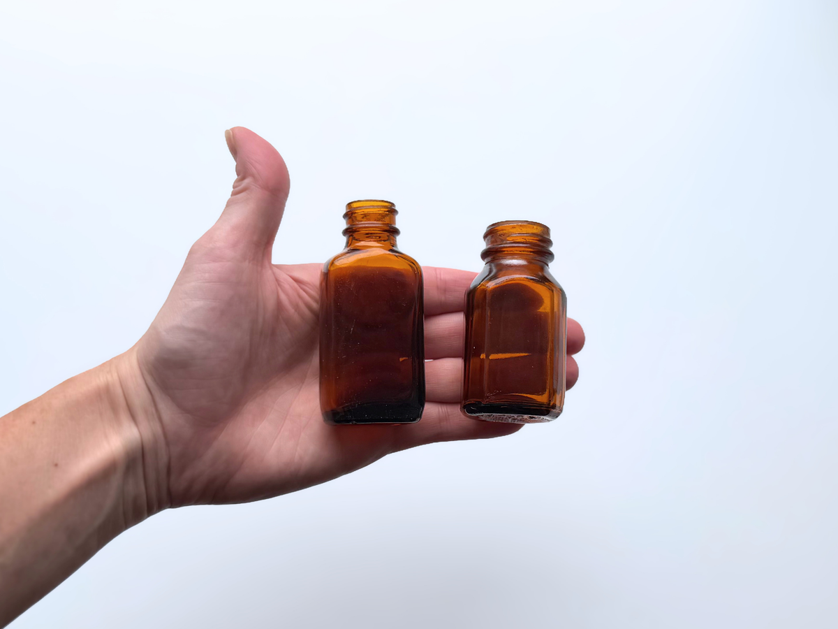 Hand holding a pair of small amber glass bottles to show scale.