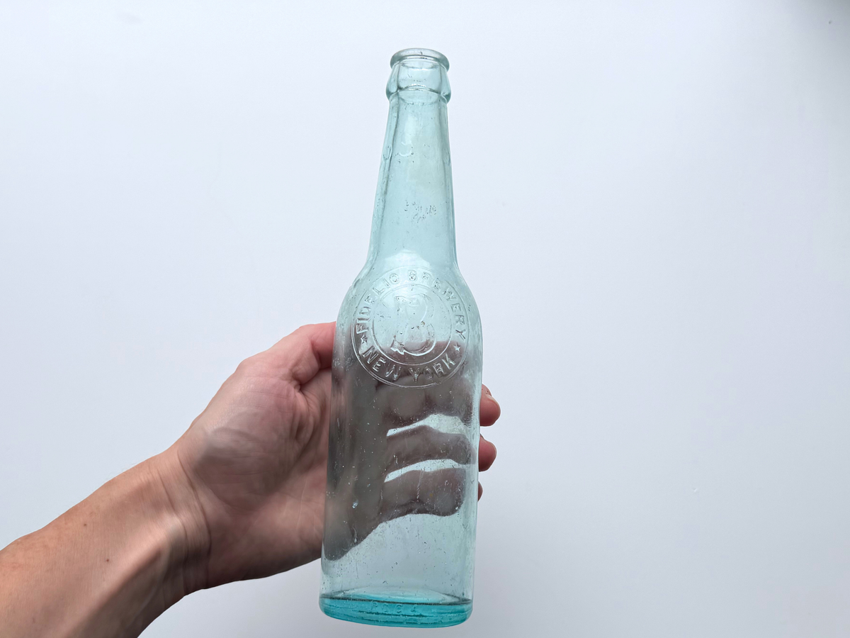 Hand holding an aqua glass Fidelio Brewery bottle to show scale and slim silhouette.