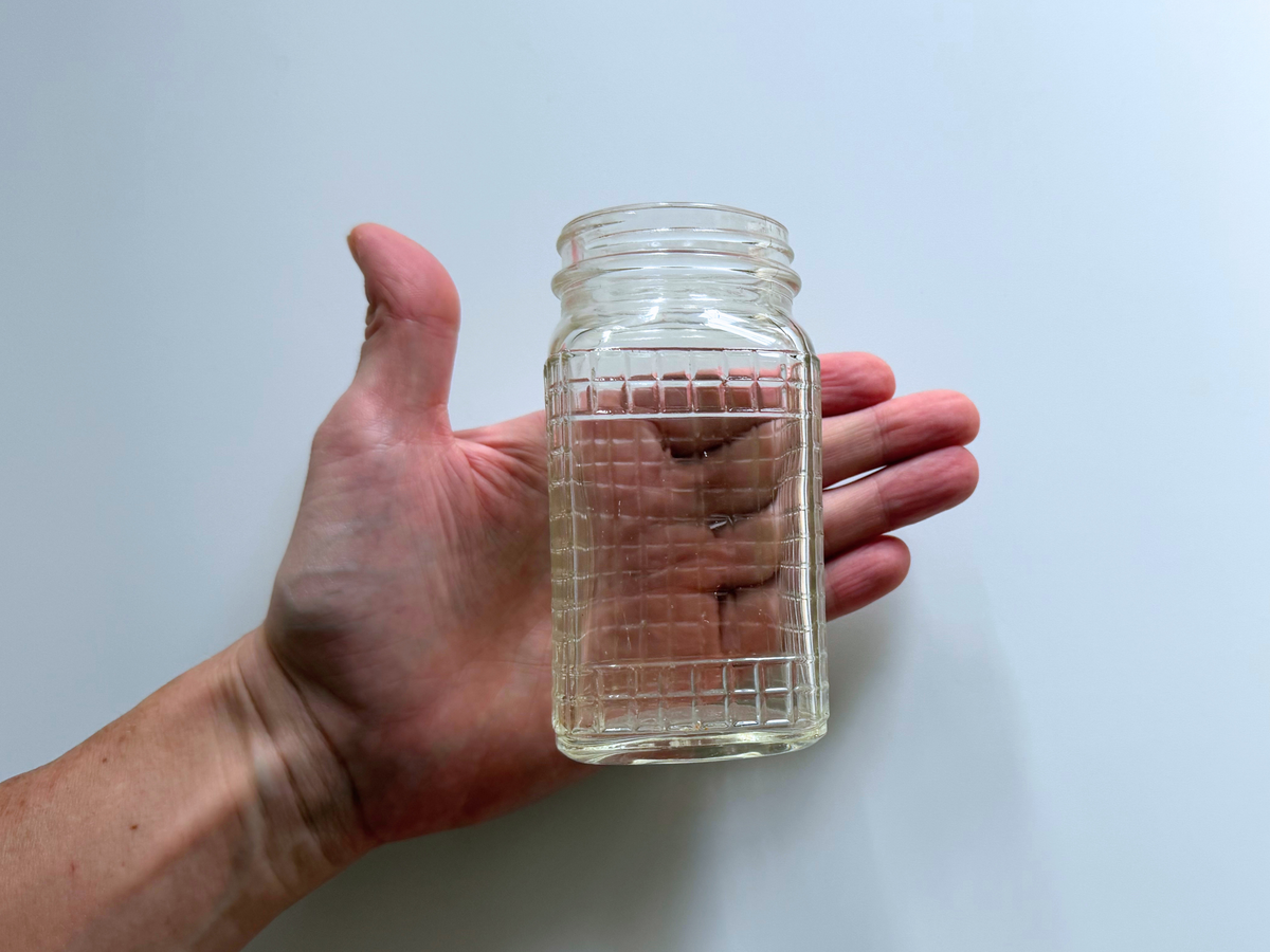 Hand holding a Ball waffle glass jar to show scale and grid texture.
