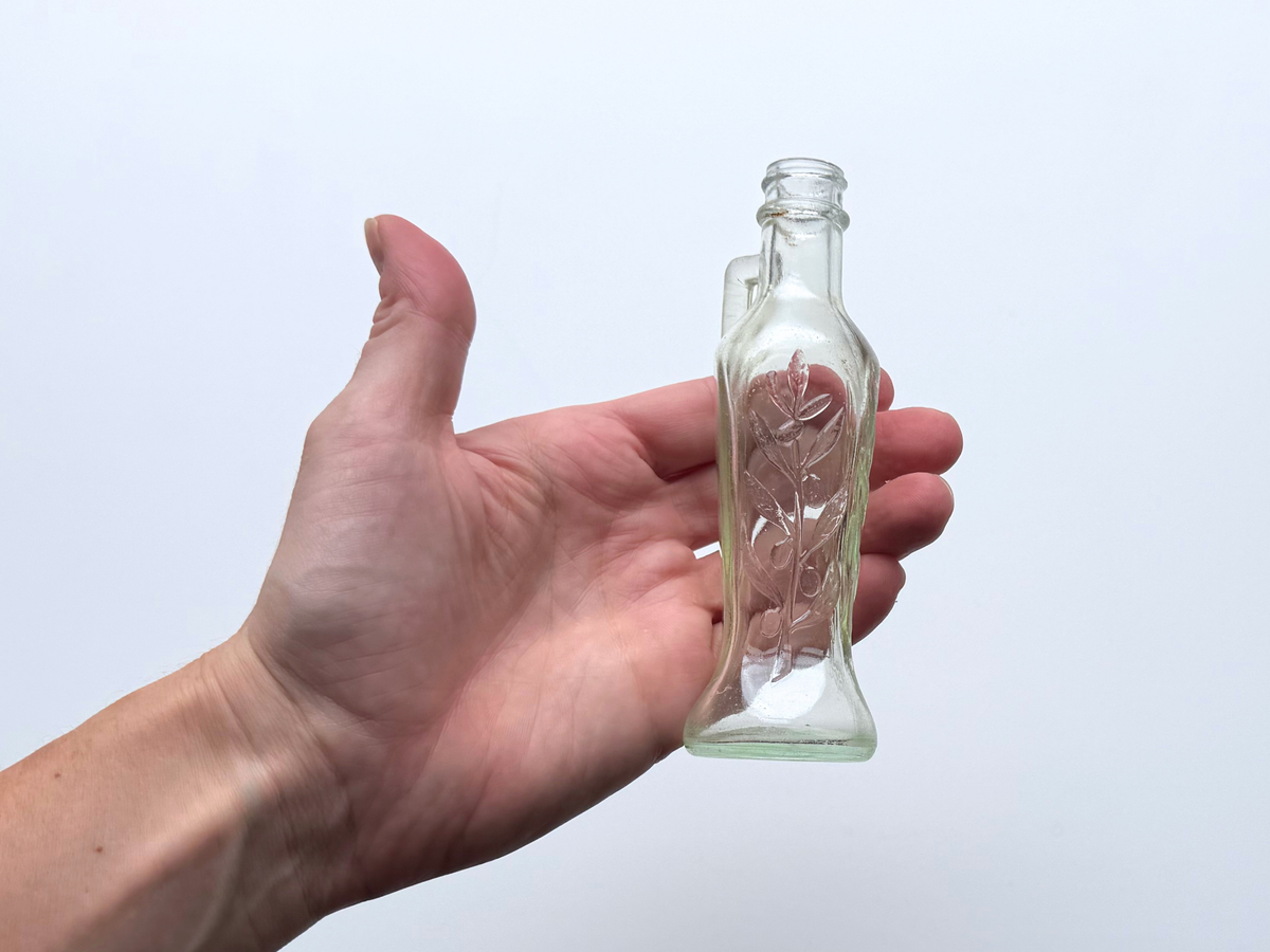 Hand holding a Bon Oil bottle to show its compact size and handle.
