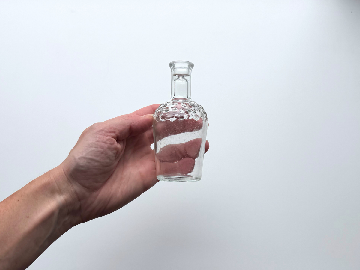Hand holding a small clear glass hobnail bud vase to show scale.