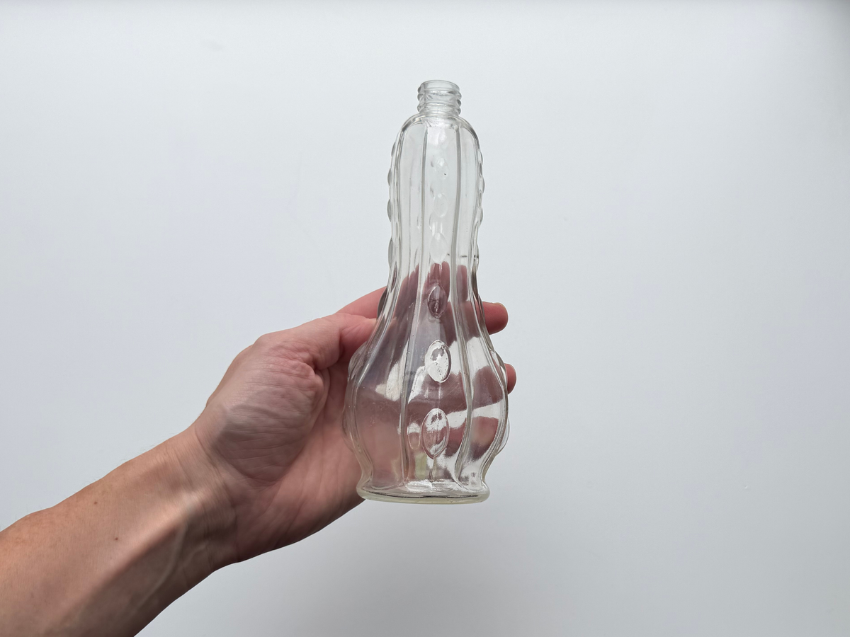 Hand holding a clear glass teardrop bottle to show its sculptural silhouette.