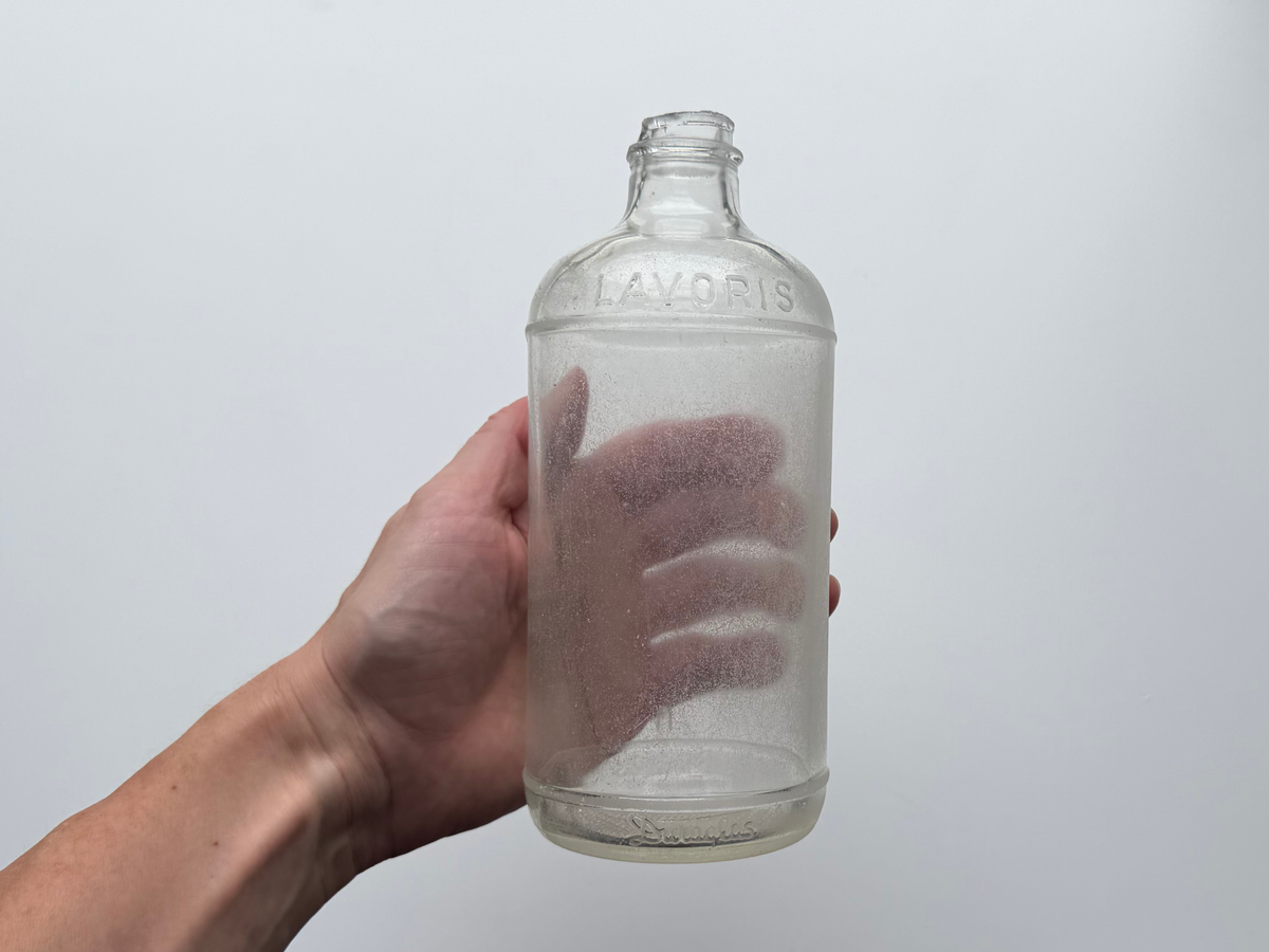 Hand holding a frosted sea glass Lavoris bottle, showing embossed LAVORIS lettering on the shoulder.