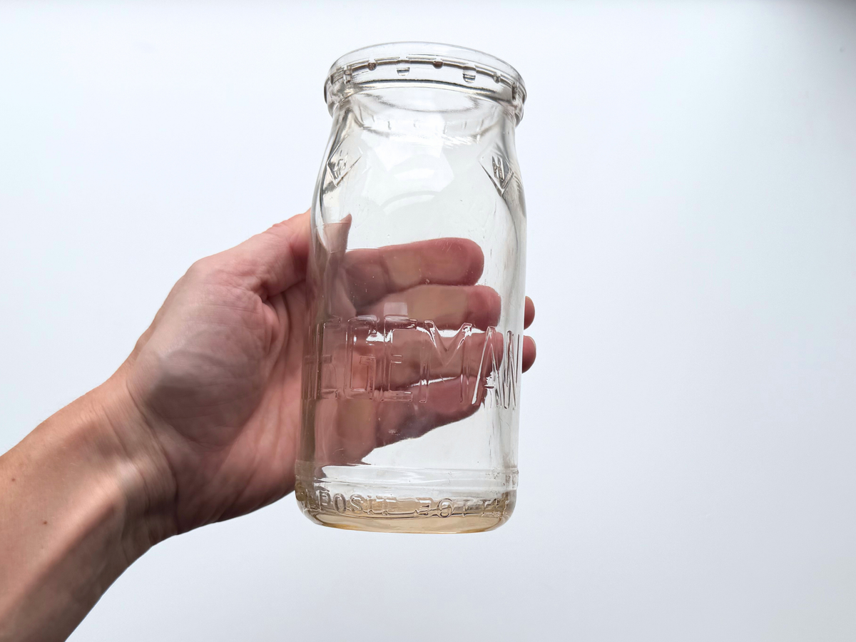 Hand holding a Hegeman Farms milk bottle to show scale and rounded shoulder.