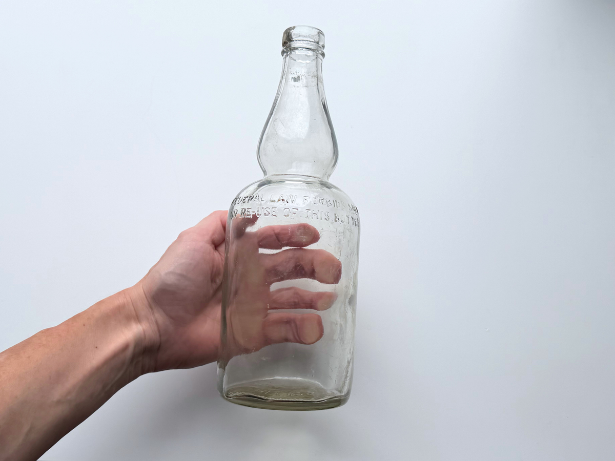 Hand holding a clear glass James Martin & Co. whiskey bottle to show scale.