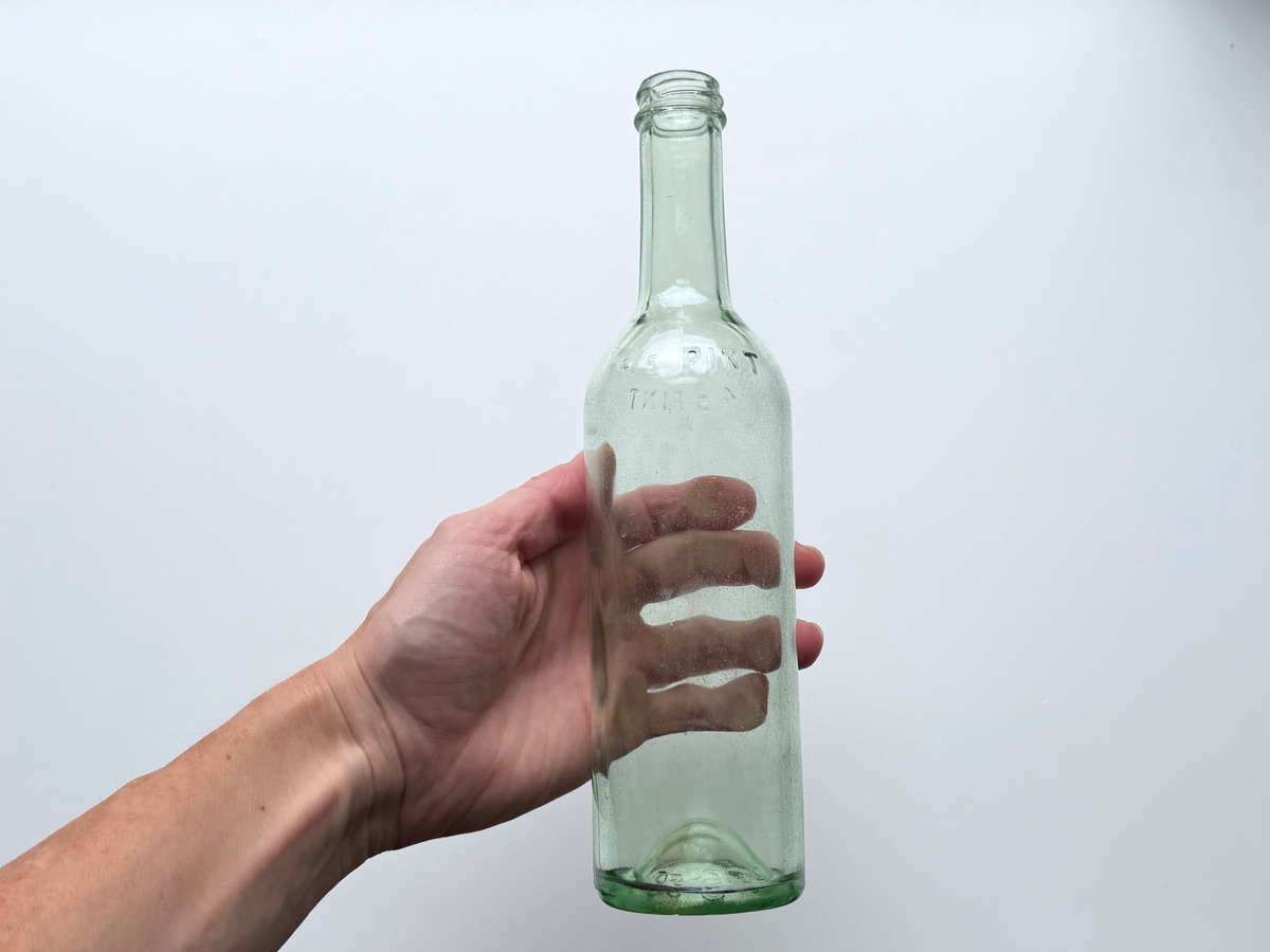 Hand holding a pale green glass bottle to show scale and slim silhouette.