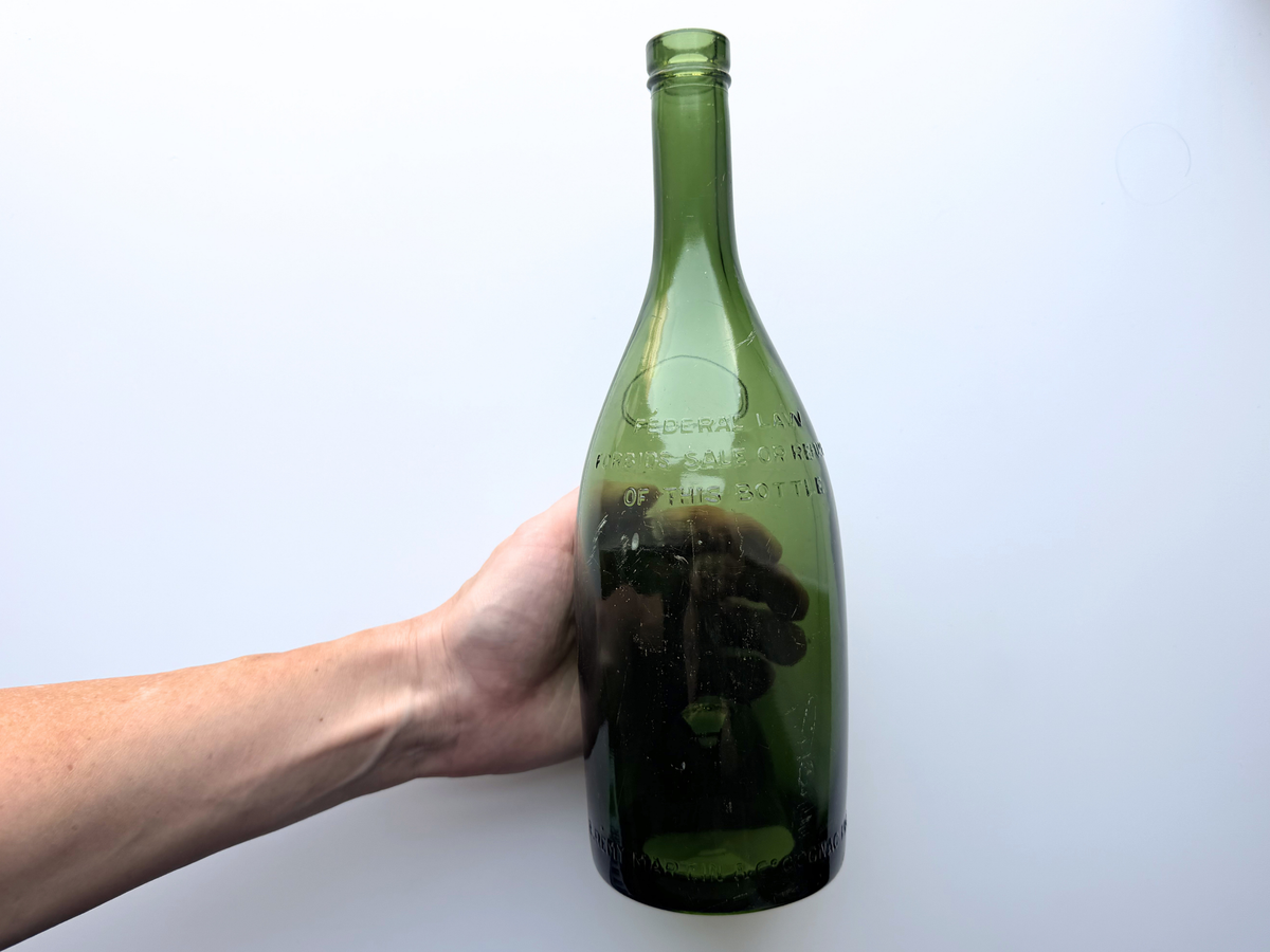 Hand holding a large green glass Remy Martin bottle to show scale.
