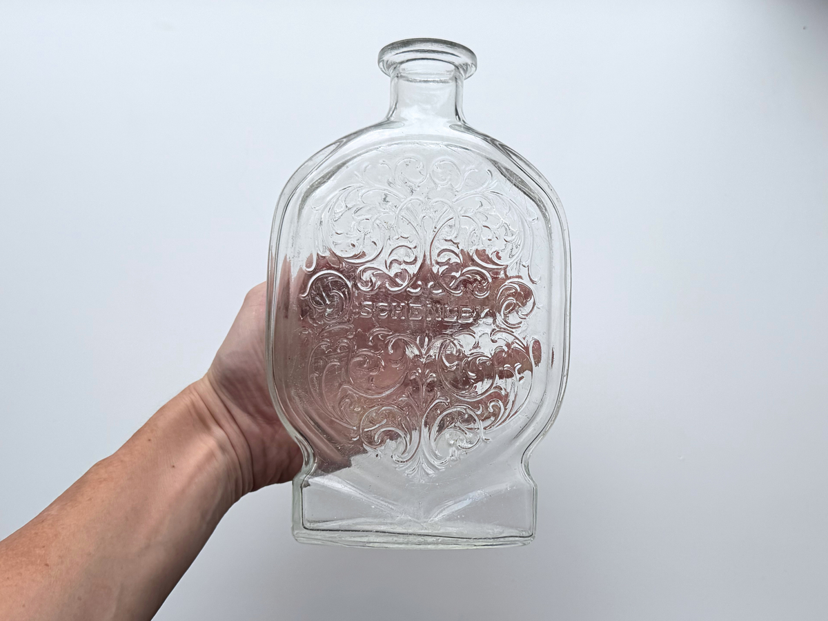 Hand holding a Schenley decanter to show its ornate scrollwork and size.