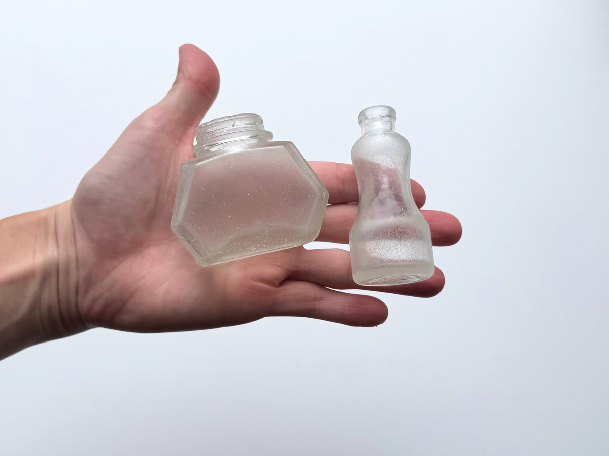 Hand holding a pair of sea-worn ink bottles to show scale and frosted texture.