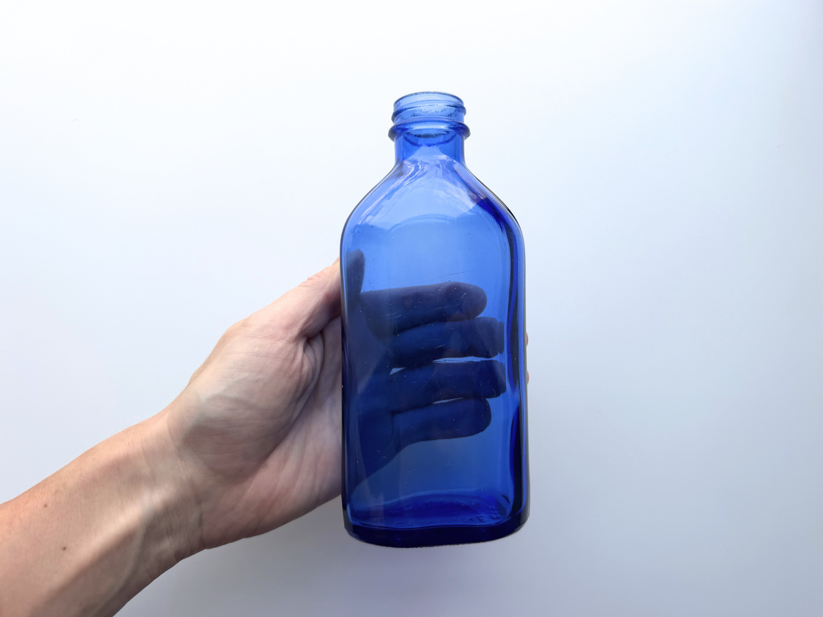 Hand holding tall Phillips cobalt blue bottle for scale