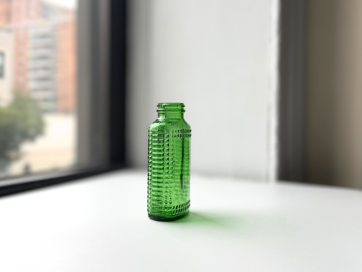 Vintage kelly green Airwick hobnail glass bottle on a windowsill, wider view