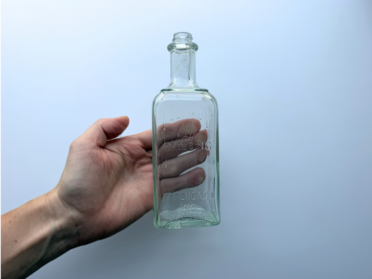 Hand holding a vintage pale greenish-blue Polymol Hair Dressing bottle to show its scale