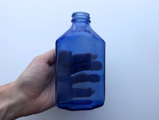 Hand holding vintage Squibb medicine bottle, showing embossed SQUIBB lettering on the front