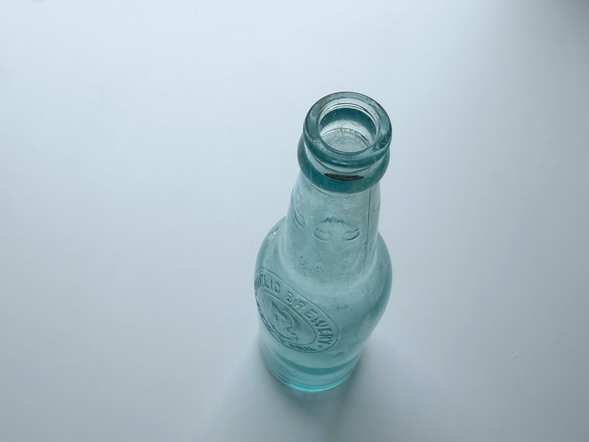Top-down view into the open mouth of an aqua glass Fidelio Brewery bottle.