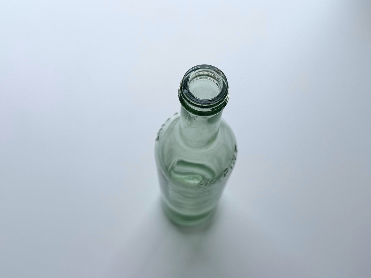 Top-down view into the open mouth of a pale green glass bottle.