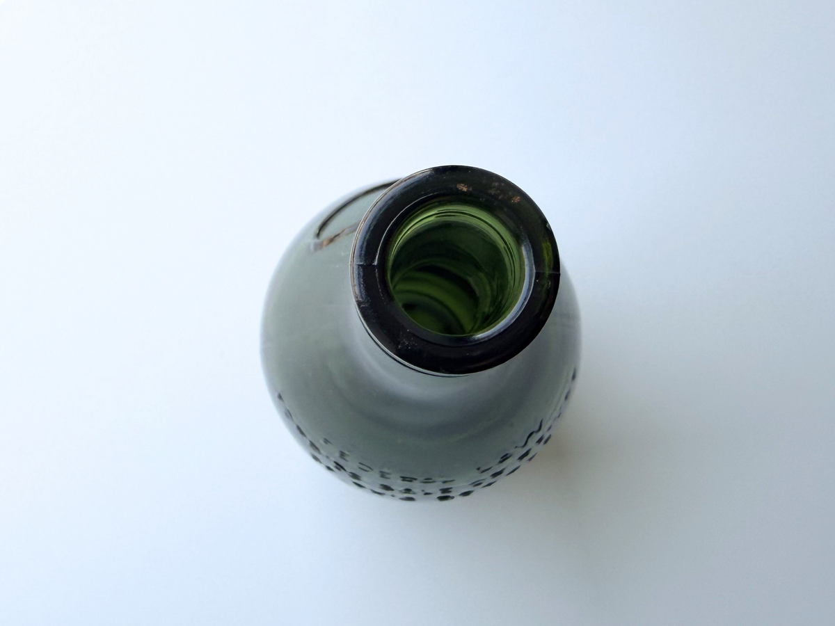 Remy Martin bottle base held in hand, showing the rounded green glass form.