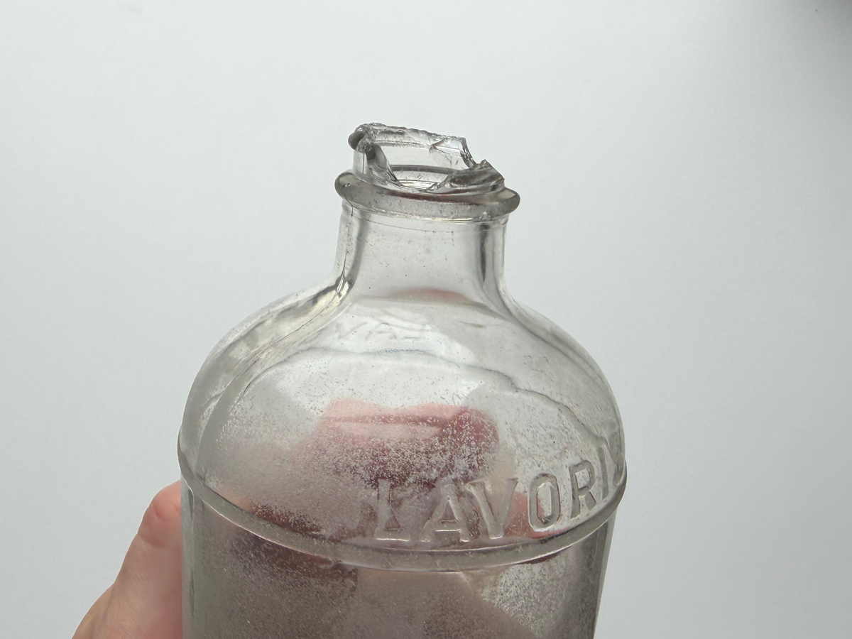 Close-up of the jagged, sea-worn mouth of a frosted vintage Lavoris bottle, smoothed by decades in the ocean.