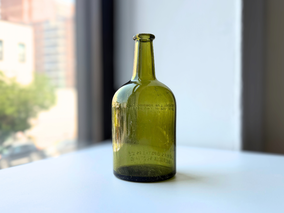 Back view of a vintage light olive green Chivas Brothers glass bottle with a long neck and dark base
