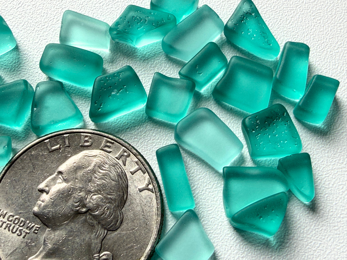 Close-up macro view of aqua micro sea glass pieces next to a quarter, showing frosted texture and shape detail.