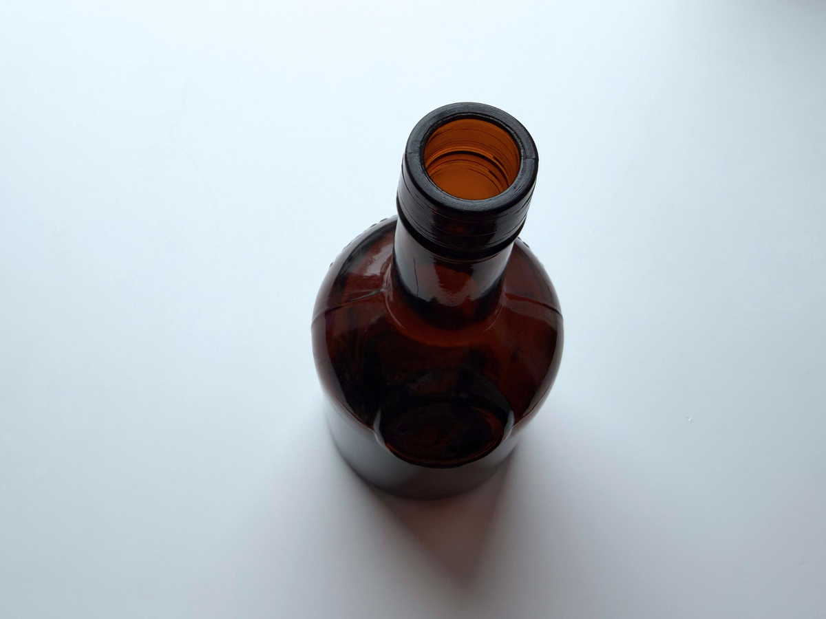 Top-down view into the open mouth of a dark amber glass bottle.