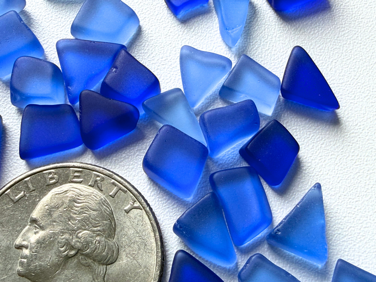 Close-up macro shot of deep blue micro sea glass pieces beside a quarter, highlighting the tiny frosted texture and true filler size of each piece.
