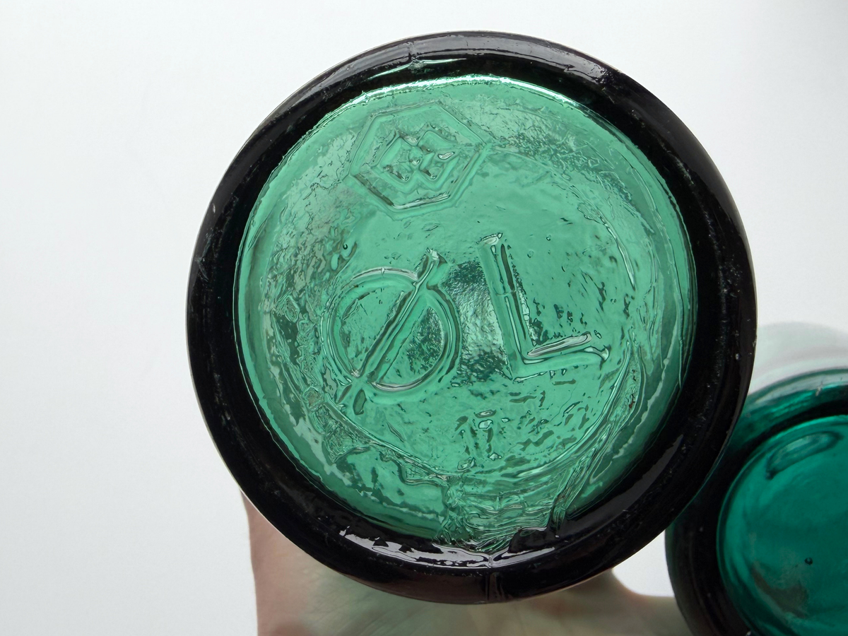 Close-up of a teal glass bottle base embossed with Kastrup Glassworks' hexagonal trademark and the Danish word OL.