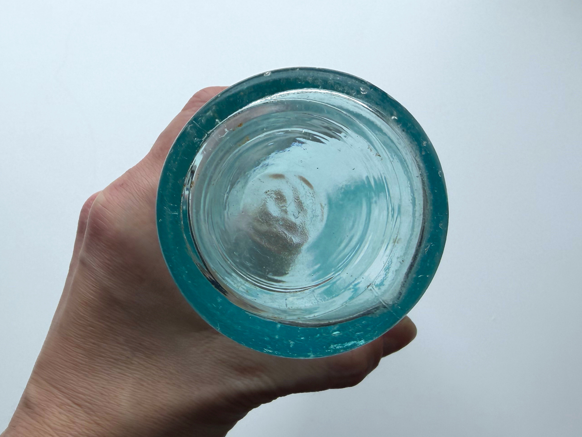 Aqua glass Fidelio Brewery bottle held in hand showing the raised circular slug plate.