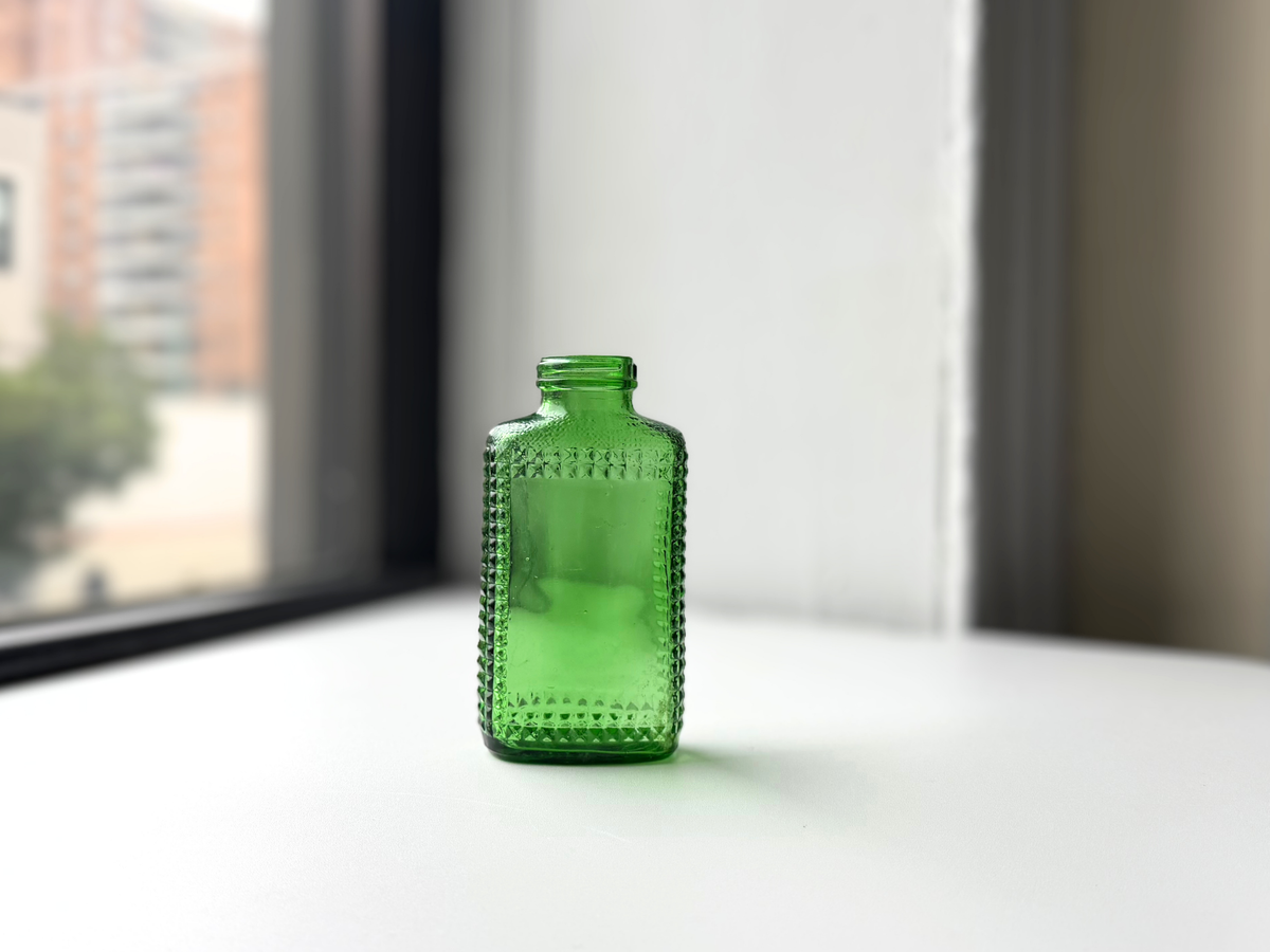 Close front view of a vintage kelly green Airwick hobnail glass bottle on a windowsill