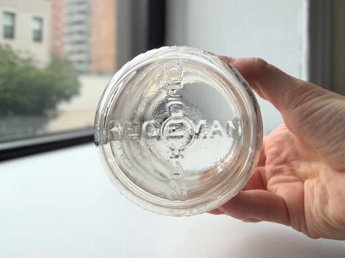 Hegeman Farms milk bottle base held in hand showing the embossed Hegeman diamond H logo.