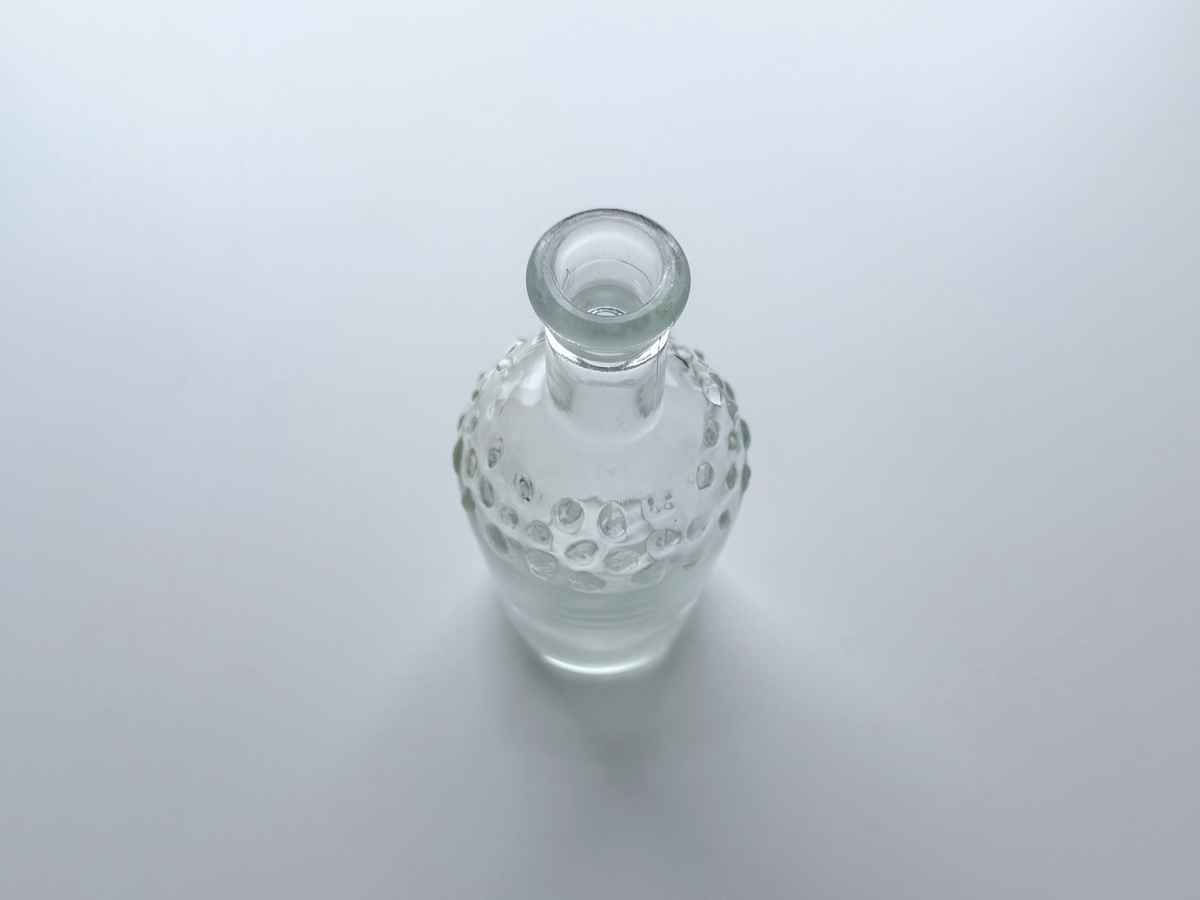 Clear glass hobnail bud vase with stopper photographed on a plain gradient background.