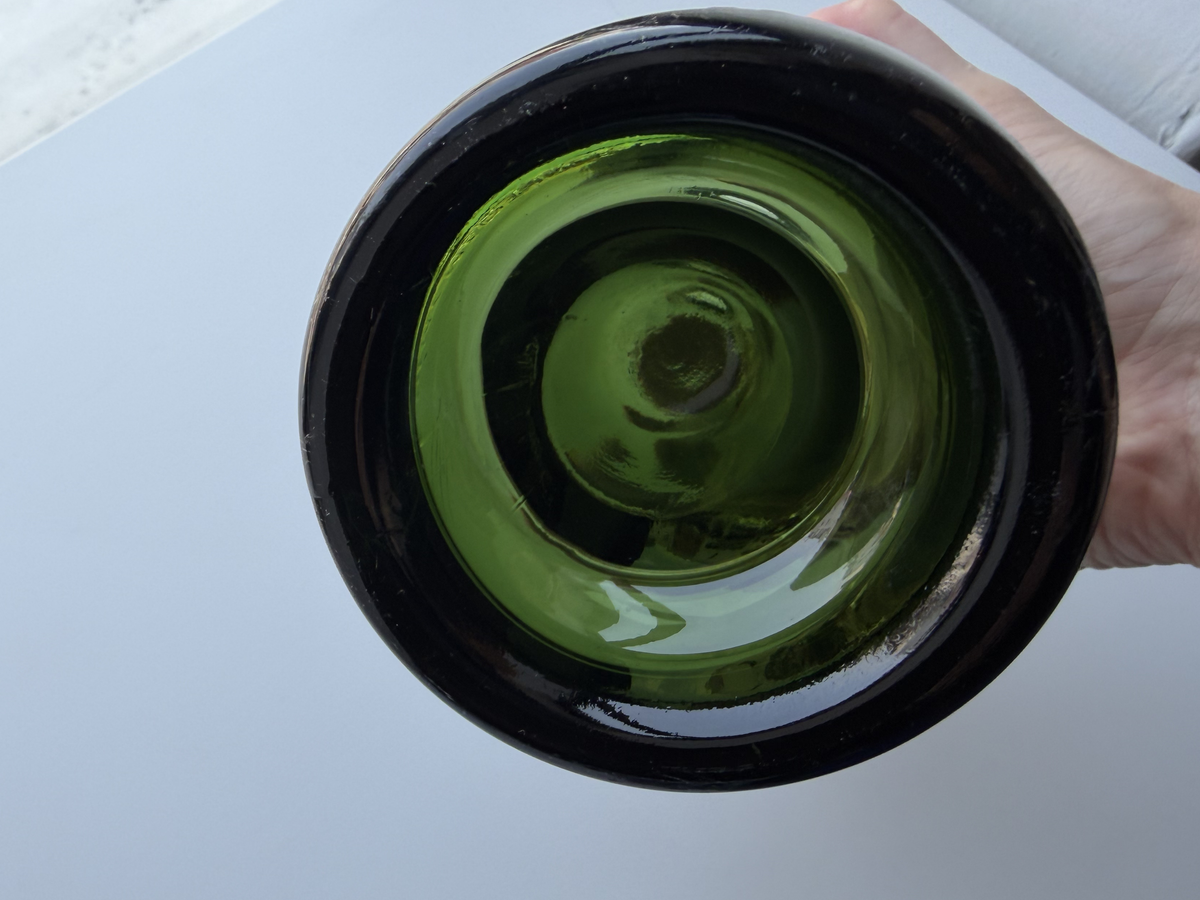 Close-up of a Remy Martin bottle base held in hand, dark green glass.