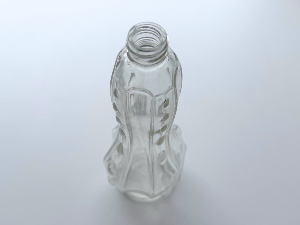 Clear glass teardrop bottle with all-over raised bump texture, photographed on a gradient background.