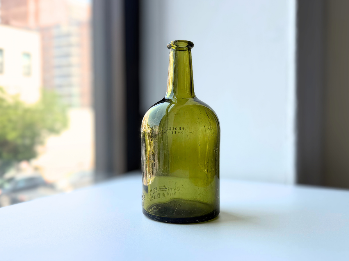 Side view of a vintage olive green glass Chivas Brothers bottle on a windowsill