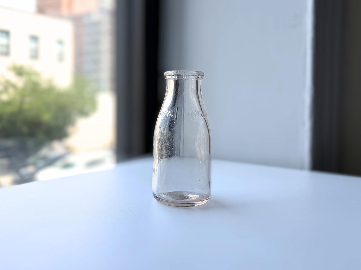 Vintage clear glass Milk for Health milk bottle, full body view against a window