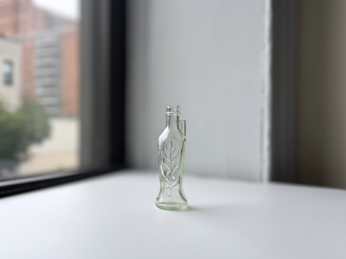 Clear glass Bon Oil bottle on a windowsill at an angle.
