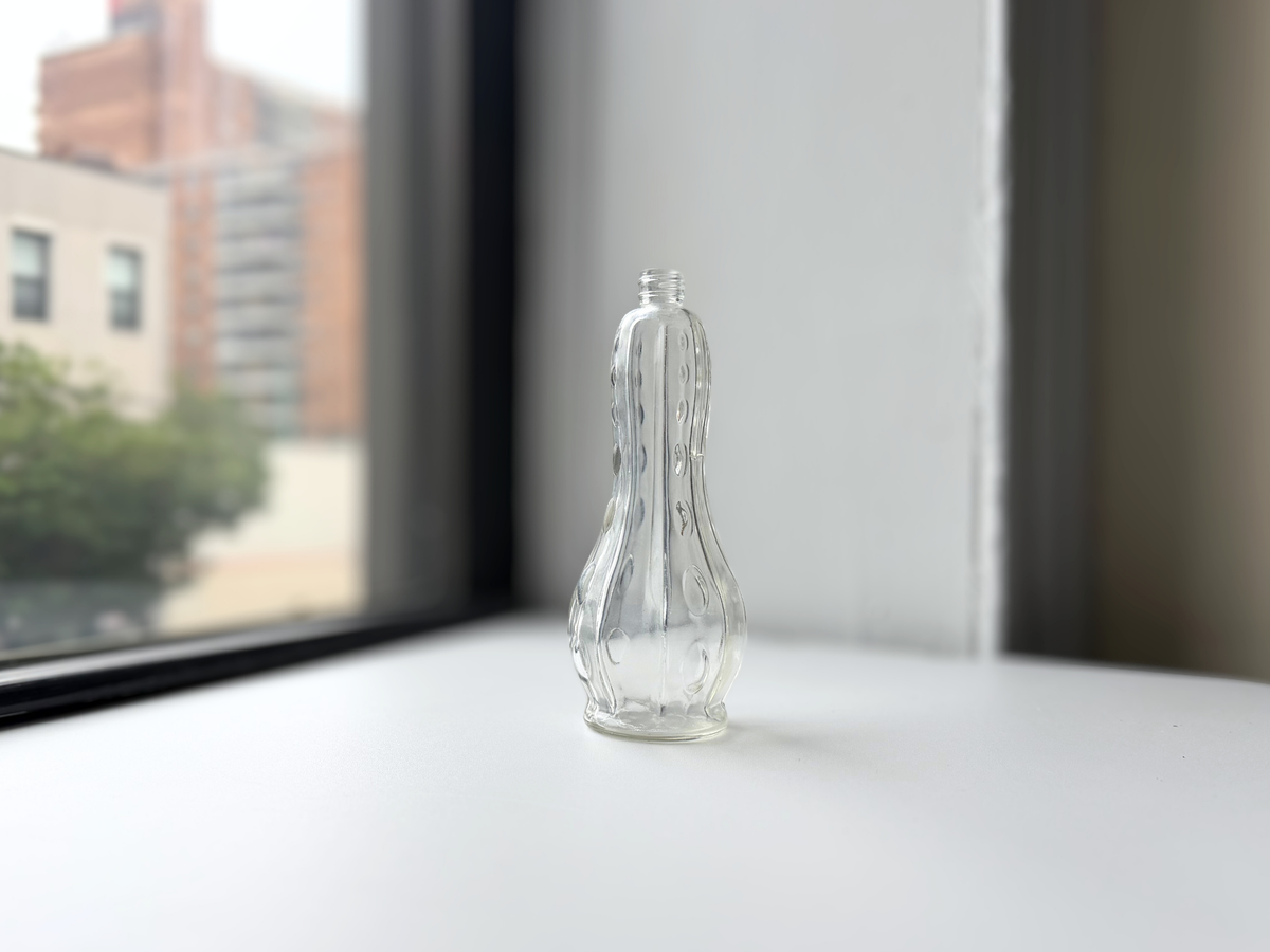 Clear glass teardrop bottle on a windowsill at an angle.