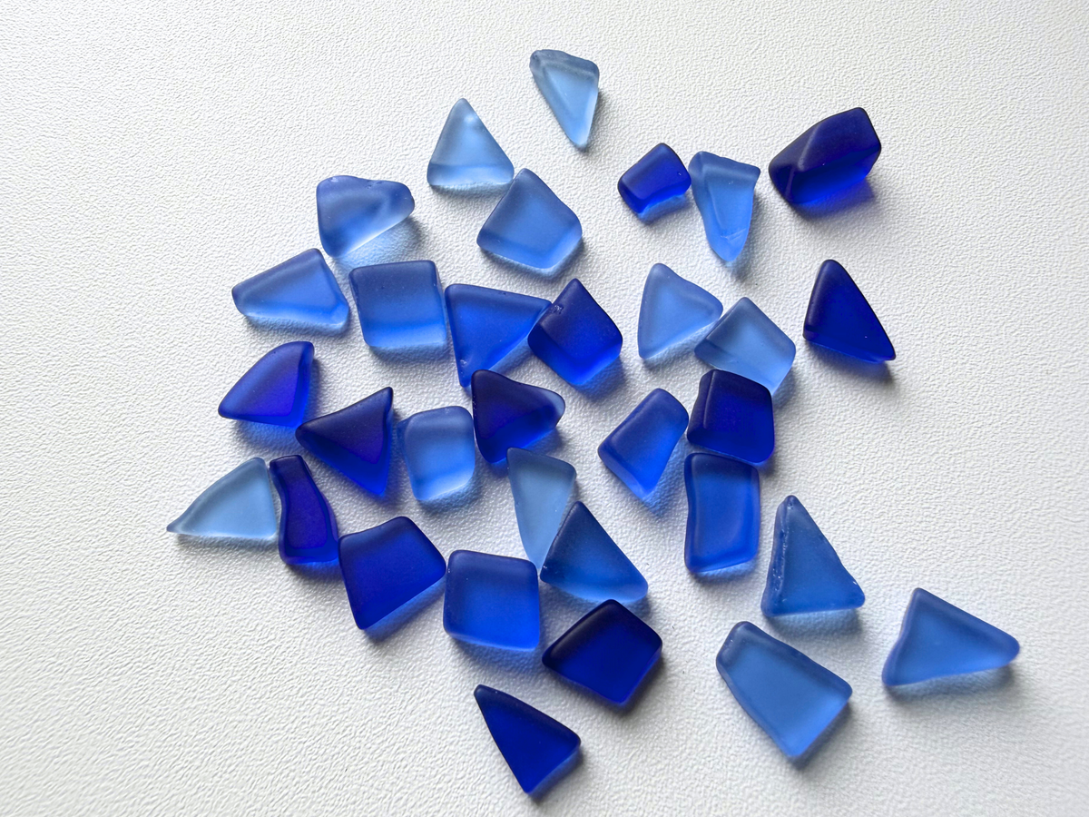 Loose pile of deep blue micro tumbled sea glass, showing the range of shapes and periwinkle-to-cobalt color variation in this filler mix.