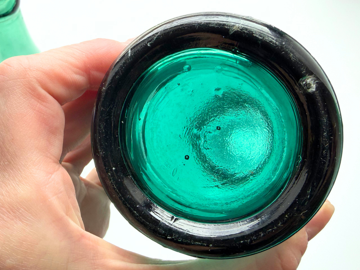 Hand holding the base of a hand-tooled antique Hamilton Glass Co. bottle, showing mold marks from manual glass finishing.