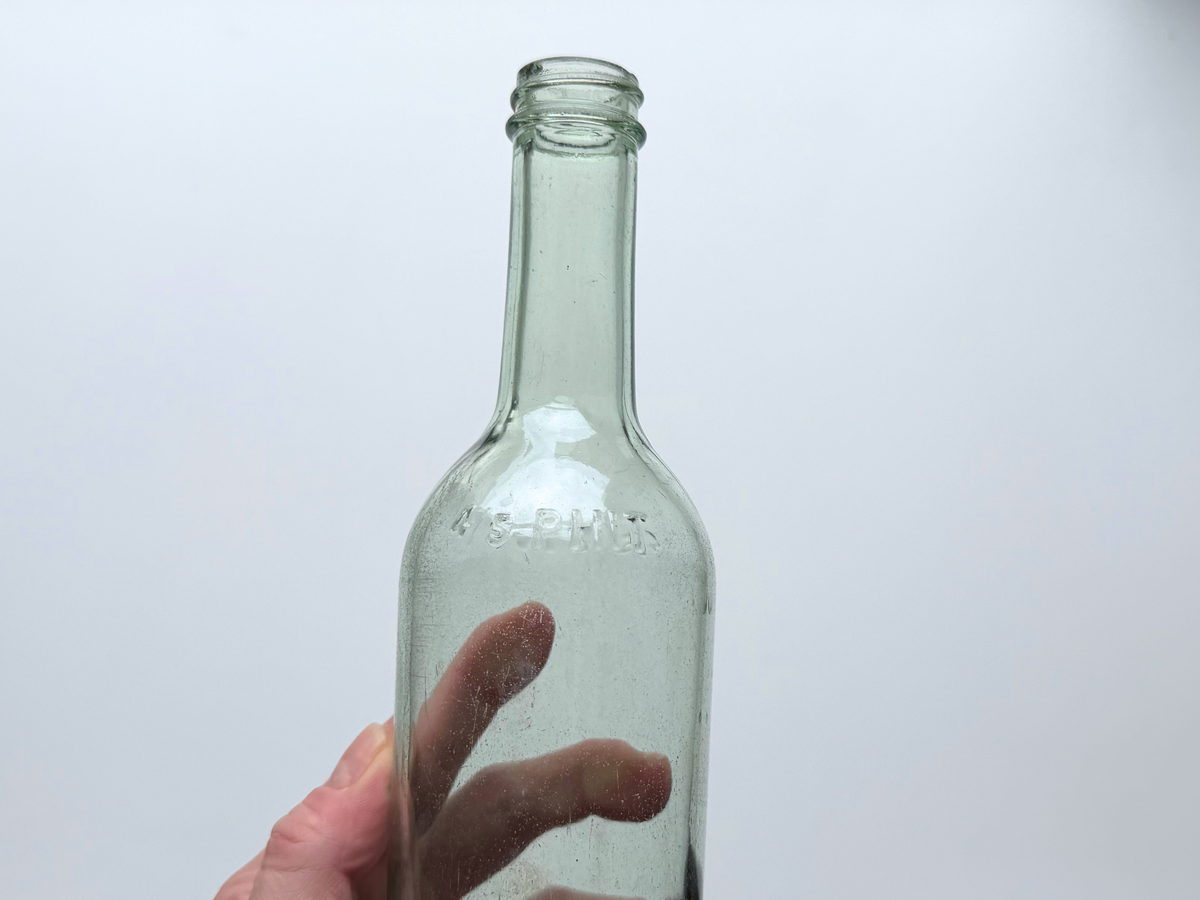 Hand holding a pale green glass bottle to show its full body and neck.