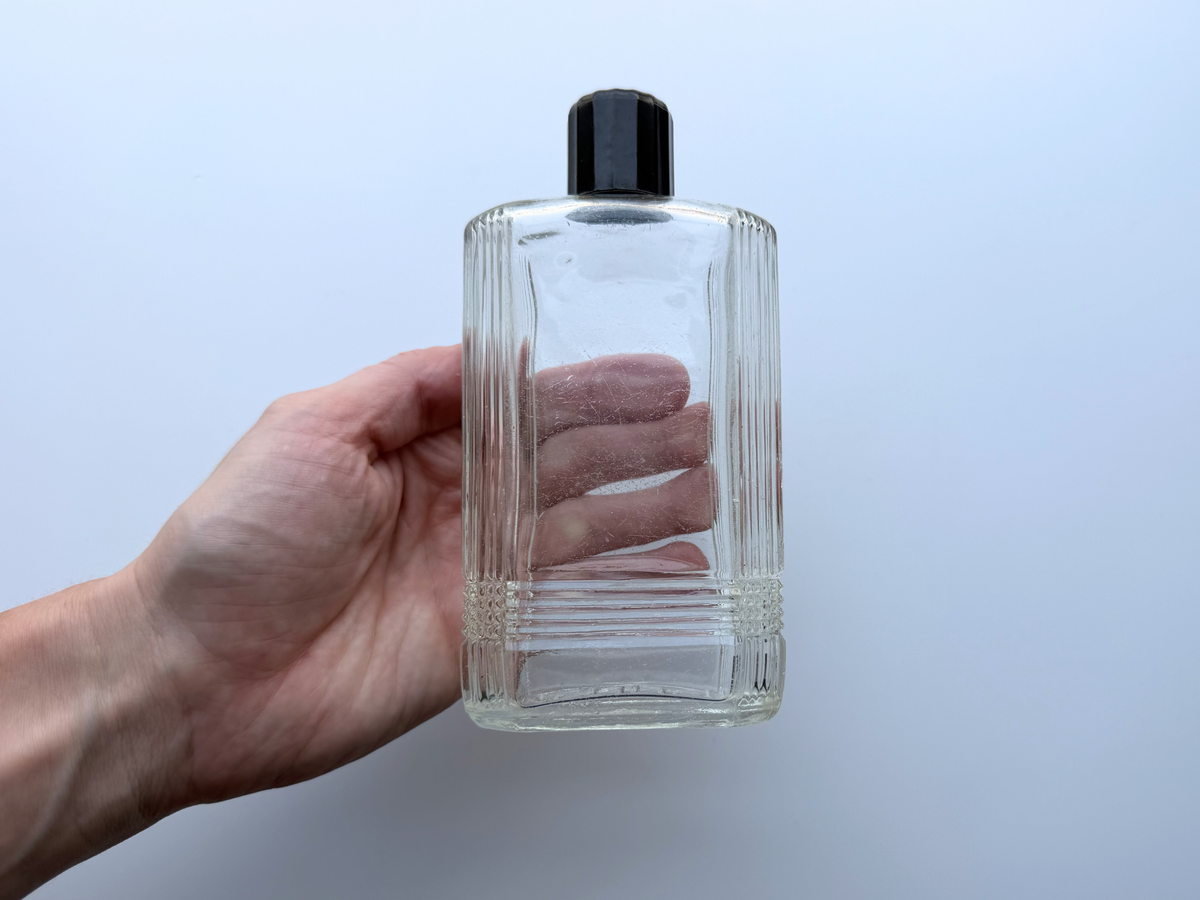 Hand holding vintage Mennen bottle for scale, clear Art Deco glass