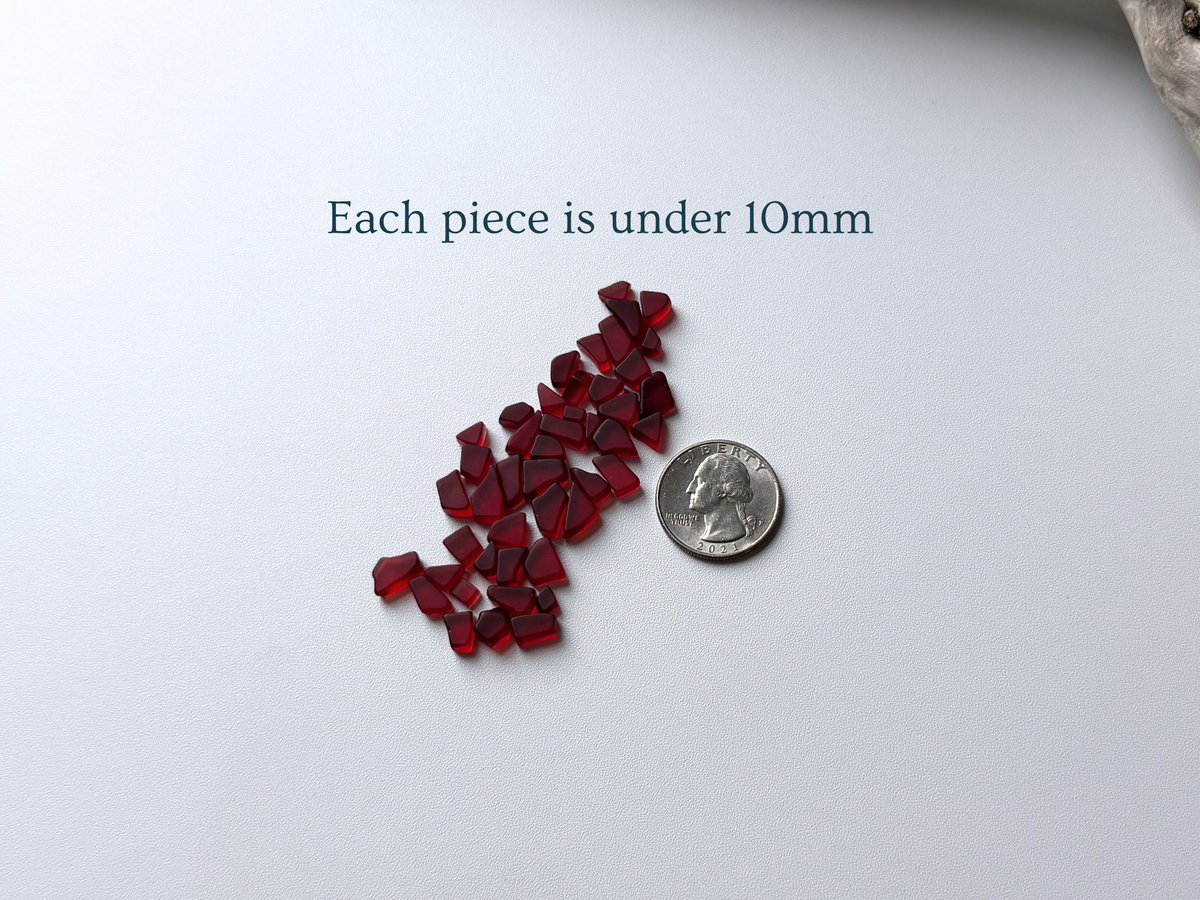 Small pile of cranberry red micro sea glass beside a quarter, with text noting each piece is under 10mm.