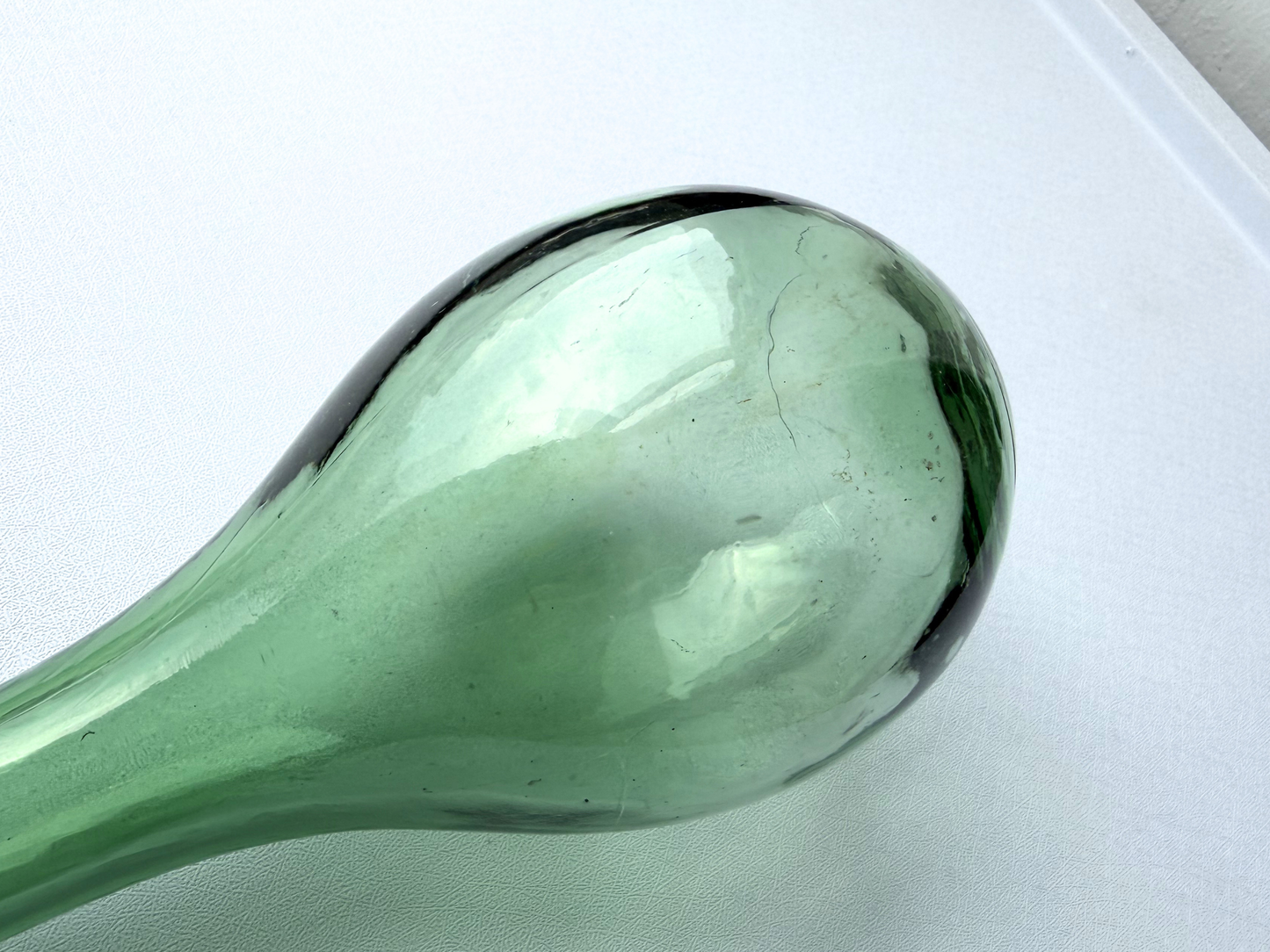 Full silhouette of a vintage green glass teardrop bottle against a plain background